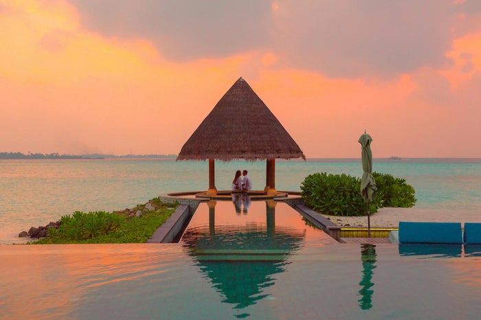 Couple sous un pavillon au bord d’une piscine à débordement au coucher du soleil