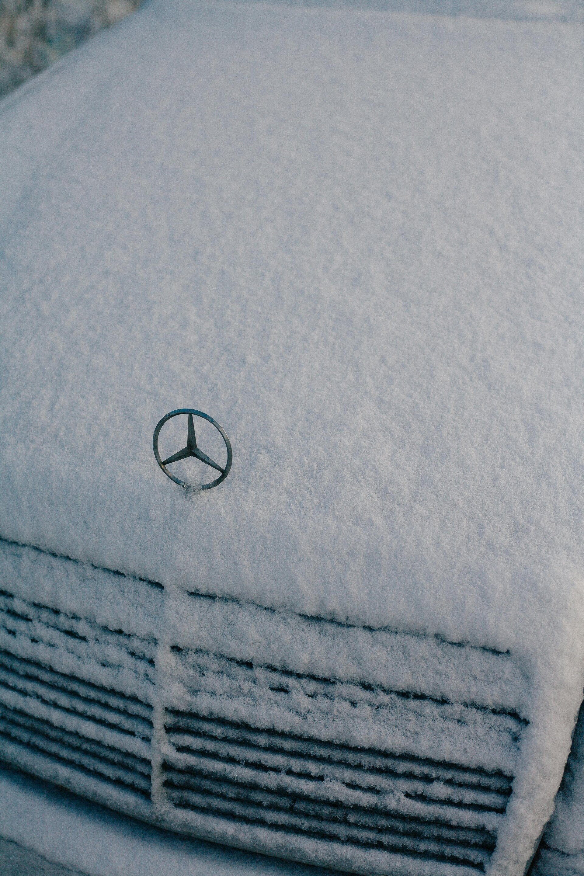 a Mercedes-Benz covered in snow with only the logo showing 