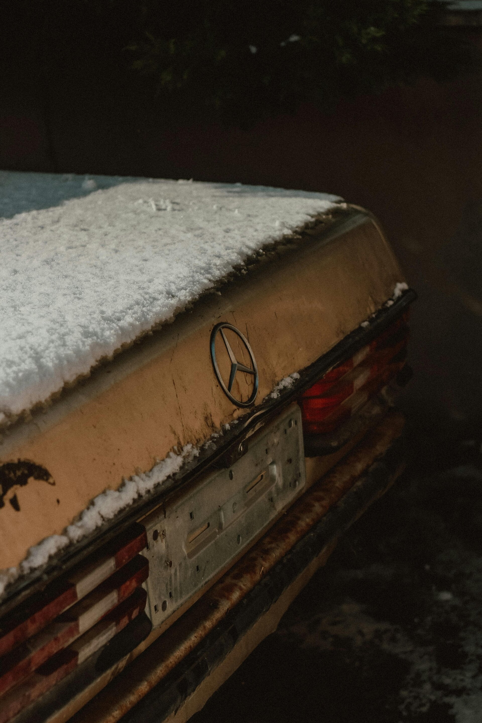 the back of an old Mercedes-Benz that has rust on it as well as snow on the top of the trunk 
