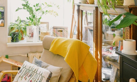 A beautifully arranged summer-inspired space, showcasing a plush chair, decorative pillows, fresh plants, and a curio cabinet with sentimental treasures