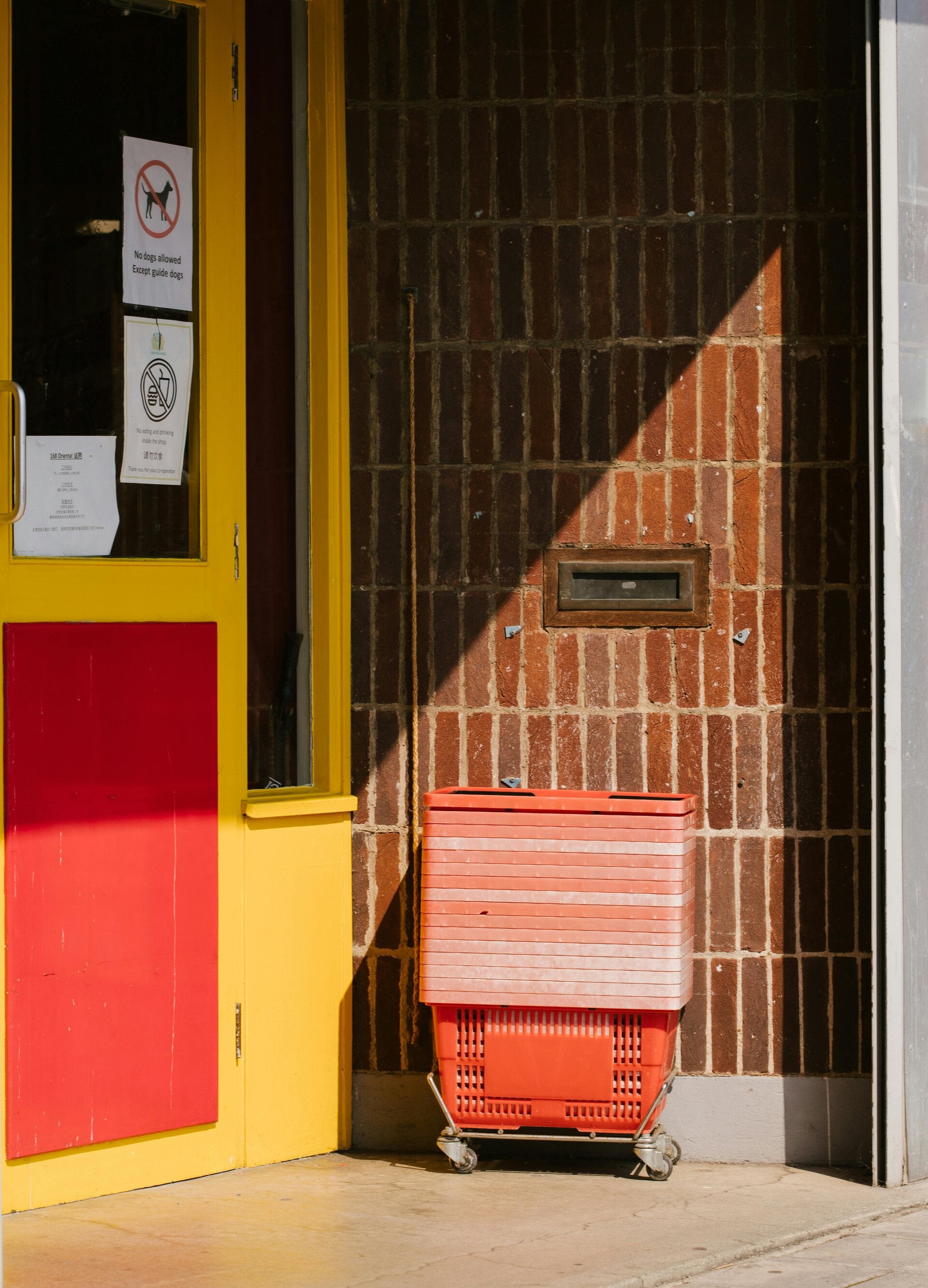 Stack of handheld shopping baskets outside a store entrance, symbolizing routine, repetition, and the weight of daily hustle.