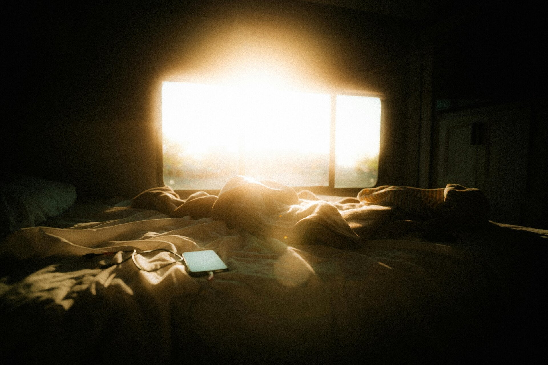 Morning sunlight piercing through open curtains in a dark bedroom, casting light over an unmade bed—symbolizing a new beginning after emotional exhaustion.