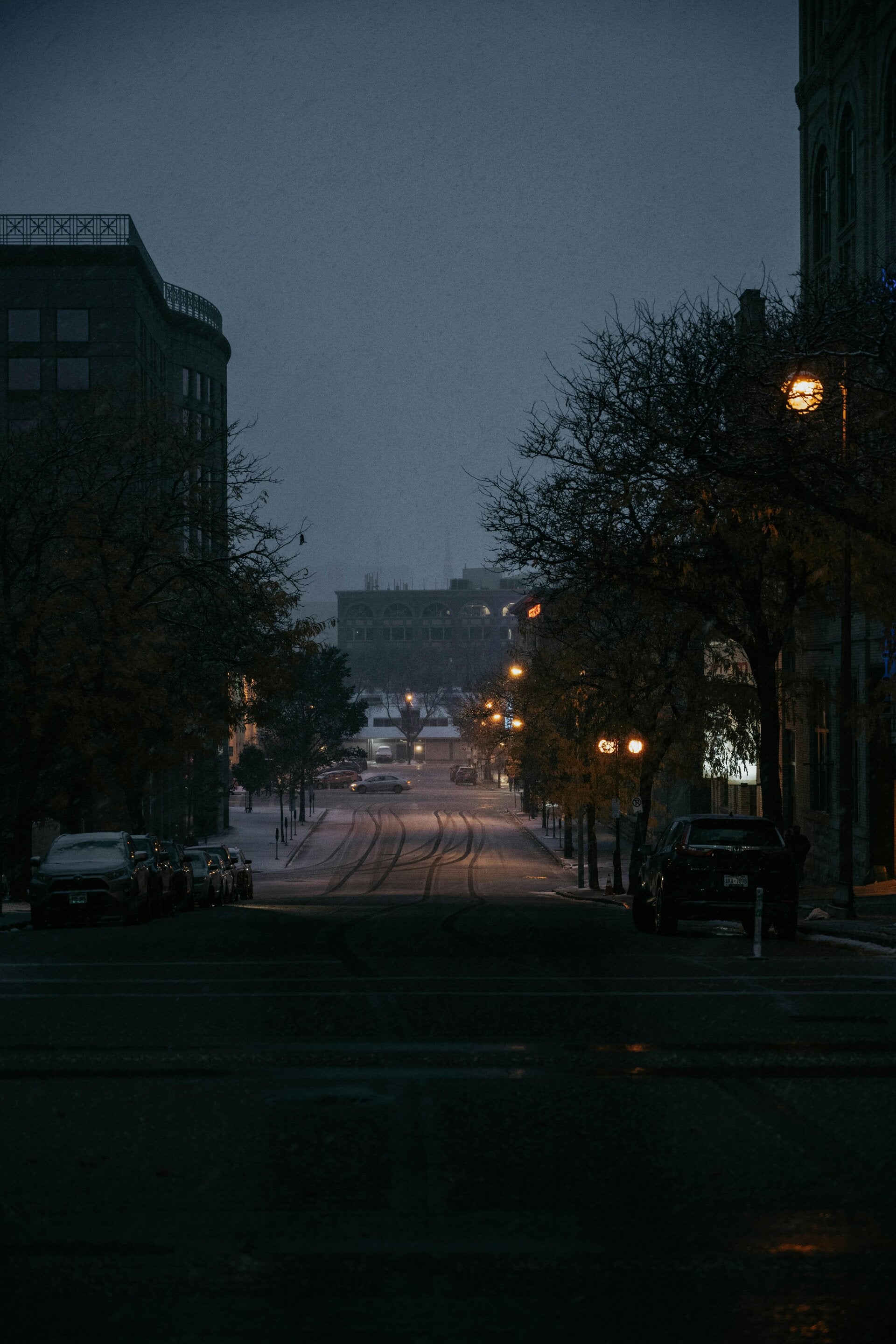 Dark, foggy street with a light snow and street lights on.
