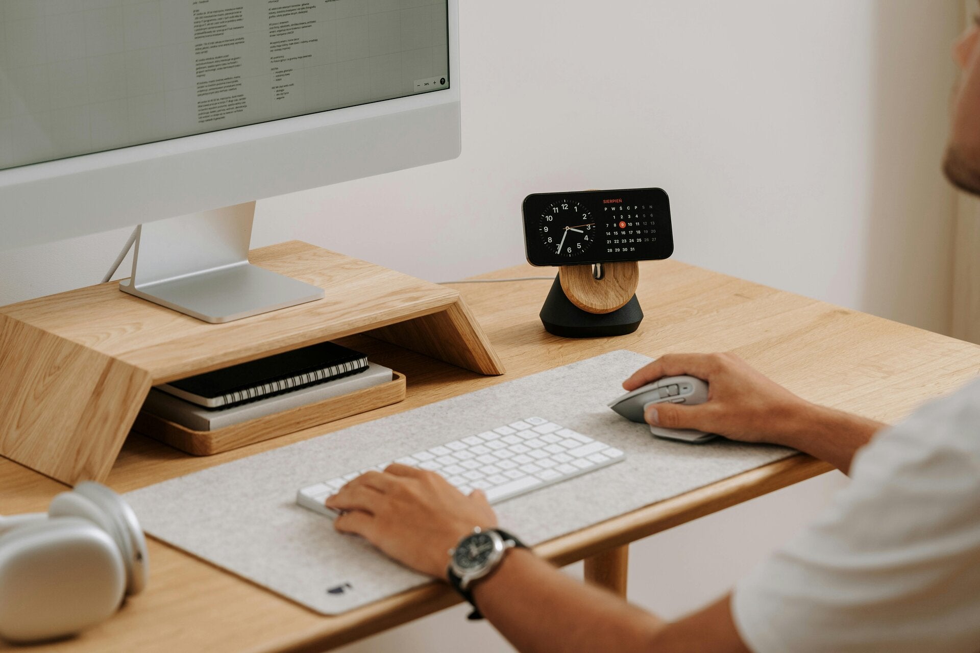 Wooden desk with a desktop computer and two hands on the desk.