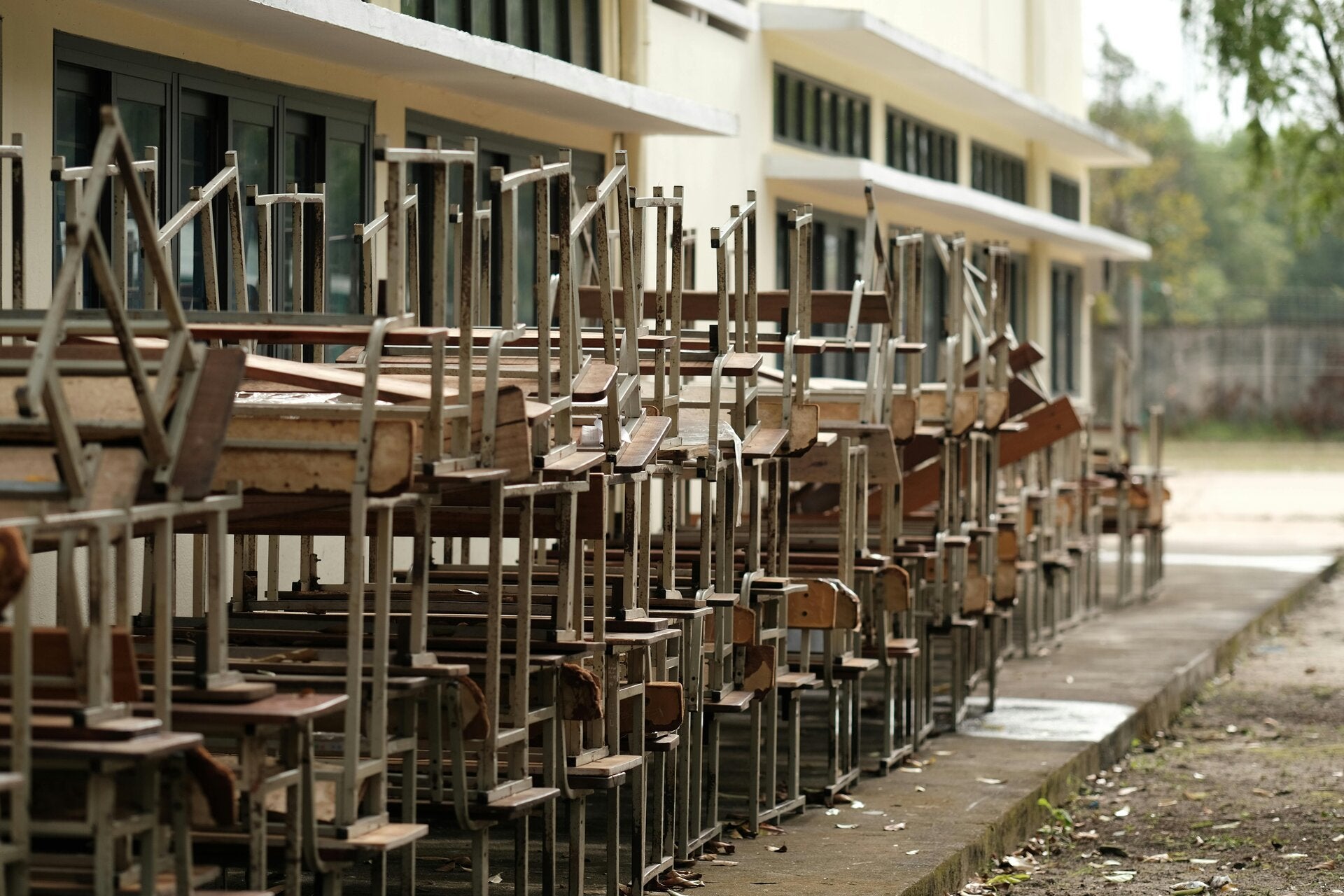 a school building in the background with a large stack of school chairs on the ground in fro of it.