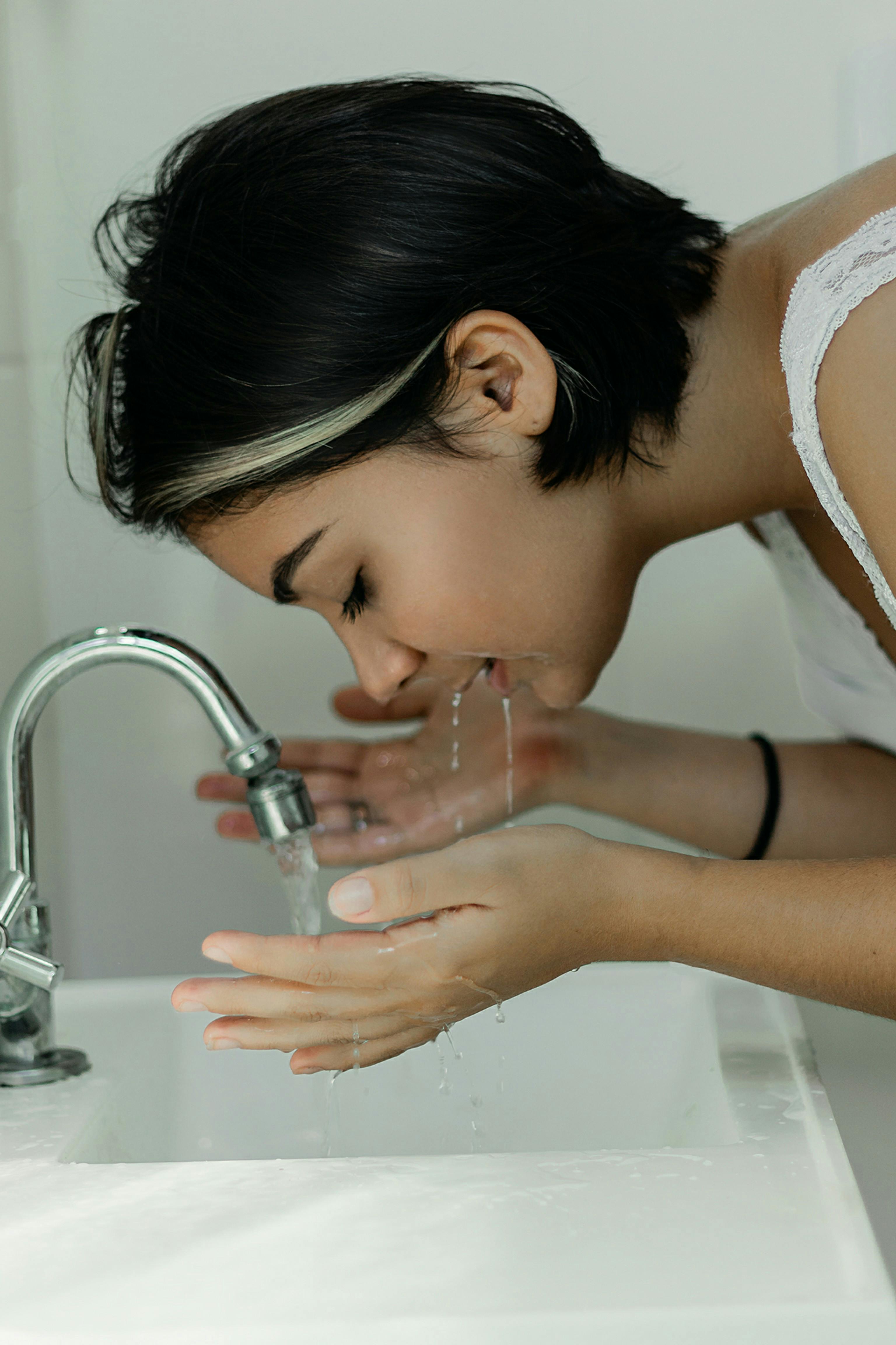 Mujer lavándose la cara con agua en el lavabo