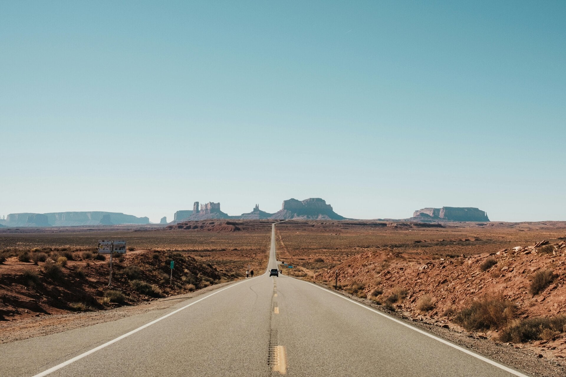 Alt= Route désertique avec Monument Valley à l’horizon dans l’Ouest américain
