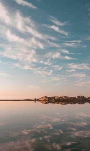 A calm scene - a body of water, hills in the distance, blue sky dotted with soft clouds