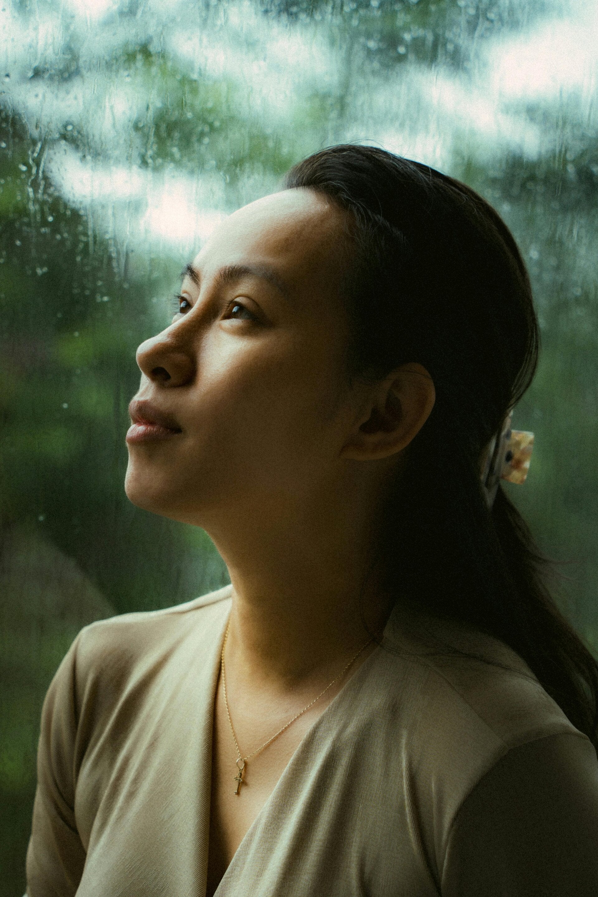 Femme pensive regardant à travers une vitre sous la pluie.