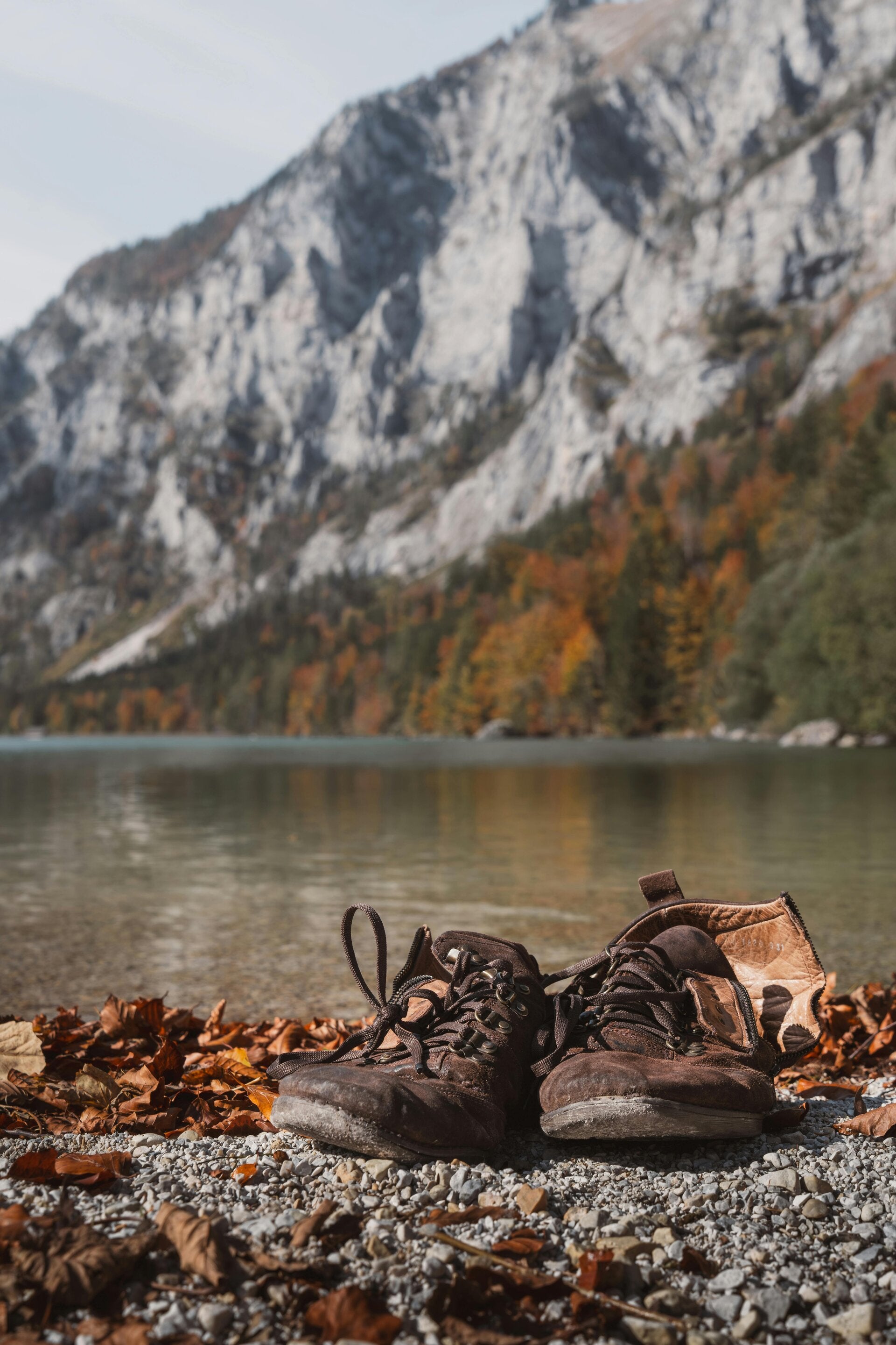 Wandelschoenen in grind met zand erop en herfstbladeren erachter