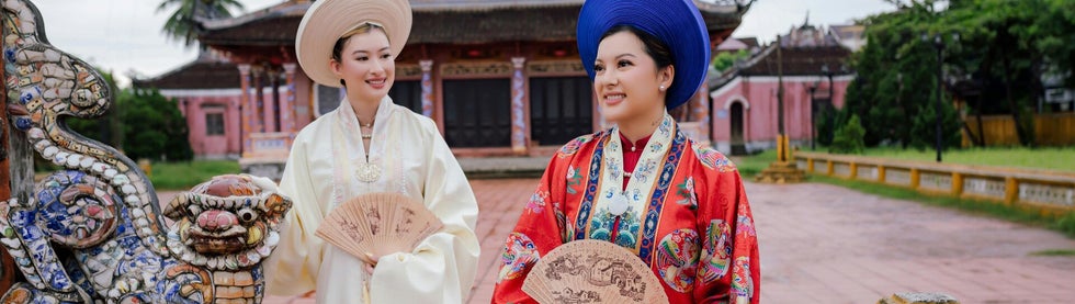 A stunning cultural moment with two women dressed in traditional garments, framed by a temple and an intricately designed dragon.