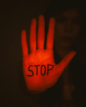 Eine rote Handinnenfläche streckt sich aufrecht dem Betrachter entgegen und trägt in schwarzer Farbe den Schriftzug "Stop".