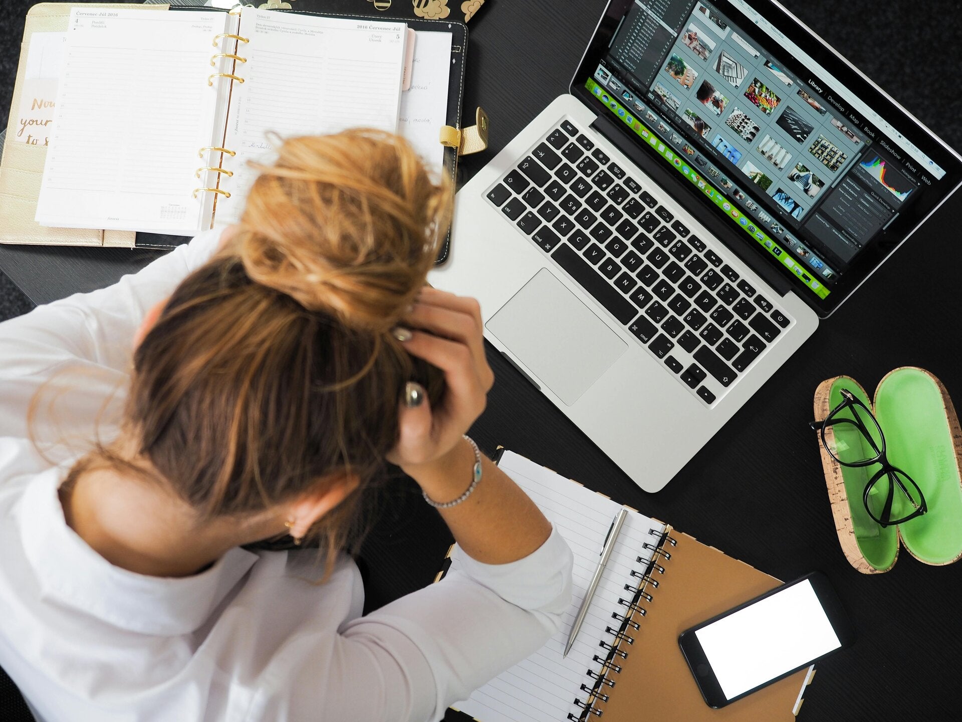 Bird’s eye view of a woman at home sitting in front of her laptop with her head in her hands, symbolizing overwhelm, burnout, or work-from-home stress.