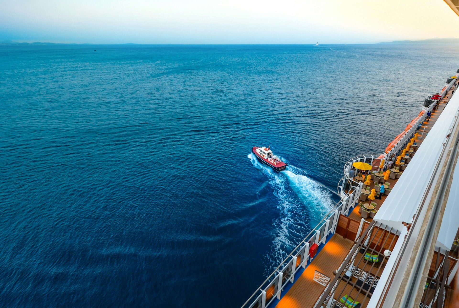 A small pilot or tender boat traveling alongside a cruise ship at sea, representing onboard safety and embarkation procedures.
