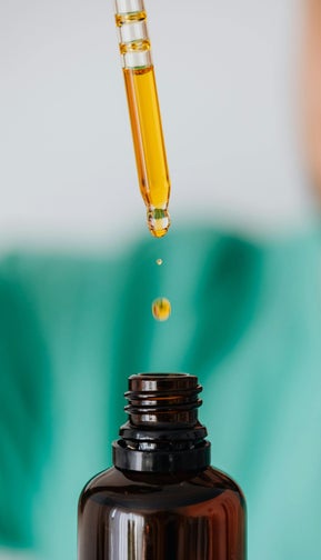 Une pipette d'huile essentielles avec une goutte qui tombe dans un flacon.