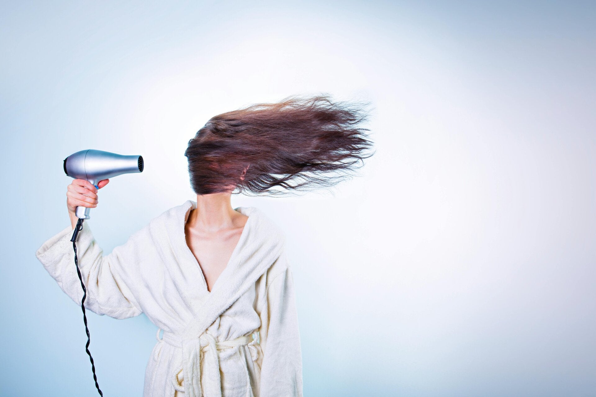 Woman blow drying her hair wearing a dressing gown