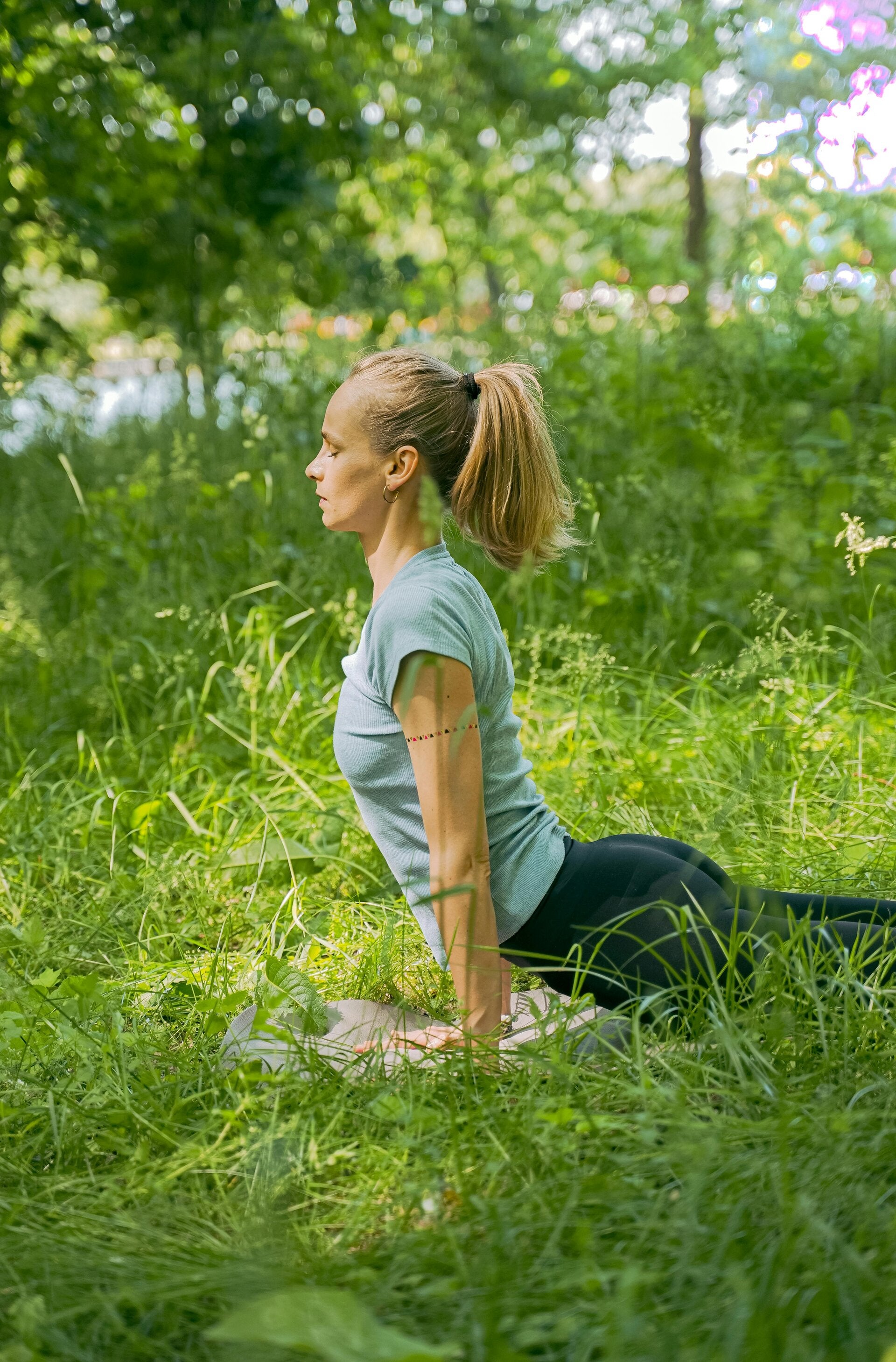 A woman practicing a simple, grounded yoga posture outdoors in a peaceful, natural setting.
