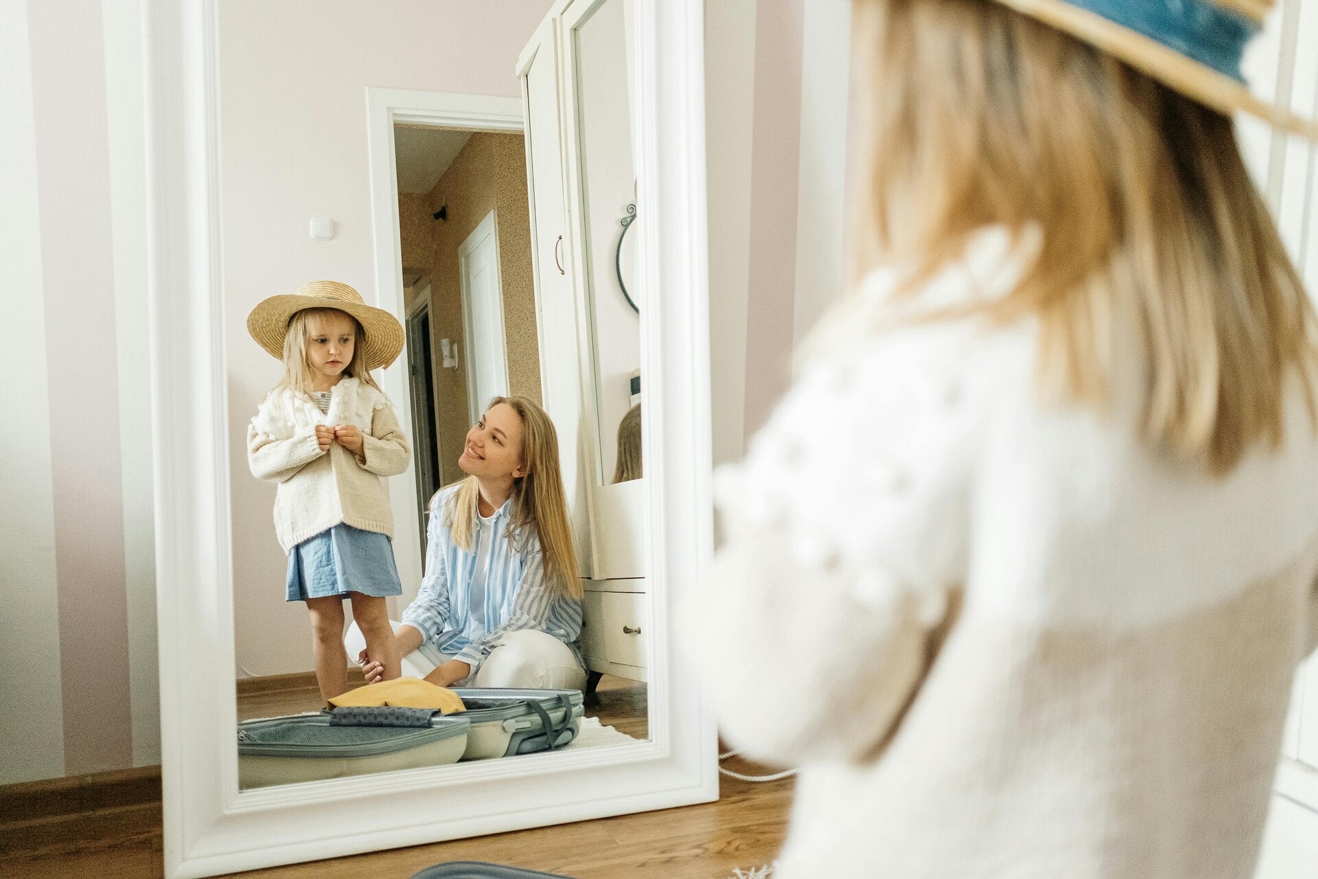 Bambina con cappello si guarda allo specchio, madre, relazione genitore-figlio.