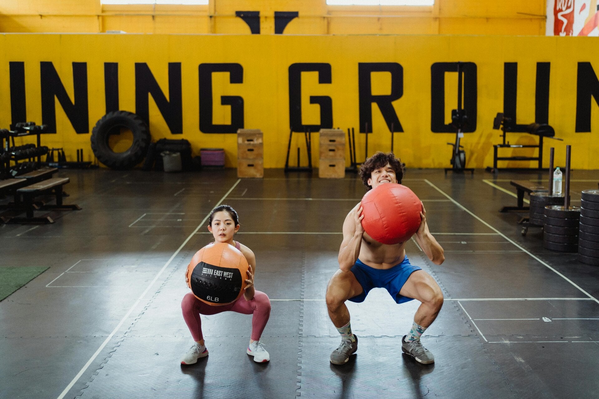 Zwei Personen machen Goblet Squats mit Medizinball in einer Trainingshalle