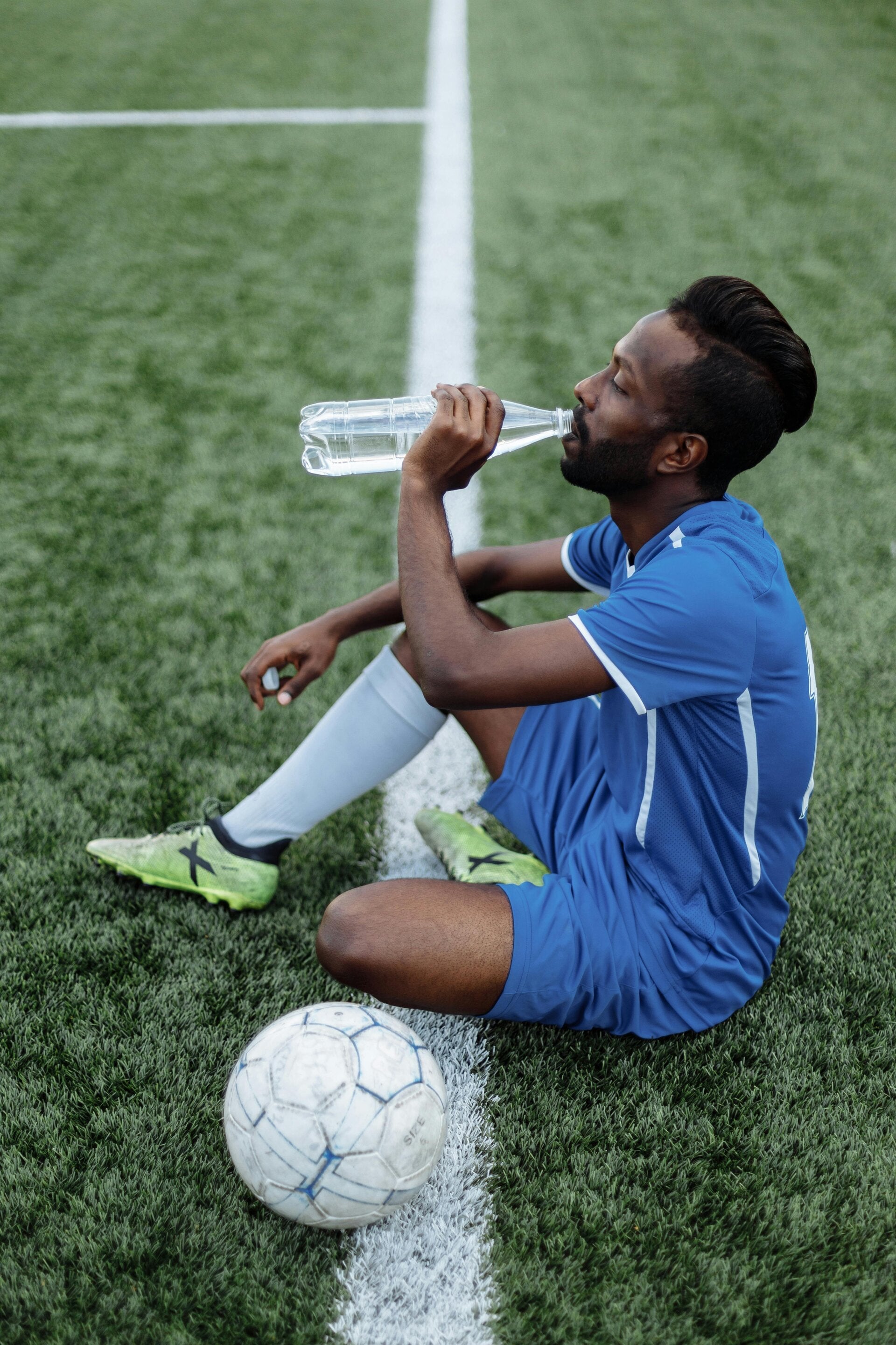 un homme en tenue de foot assis au sol en train de boire une bouteille d'eau