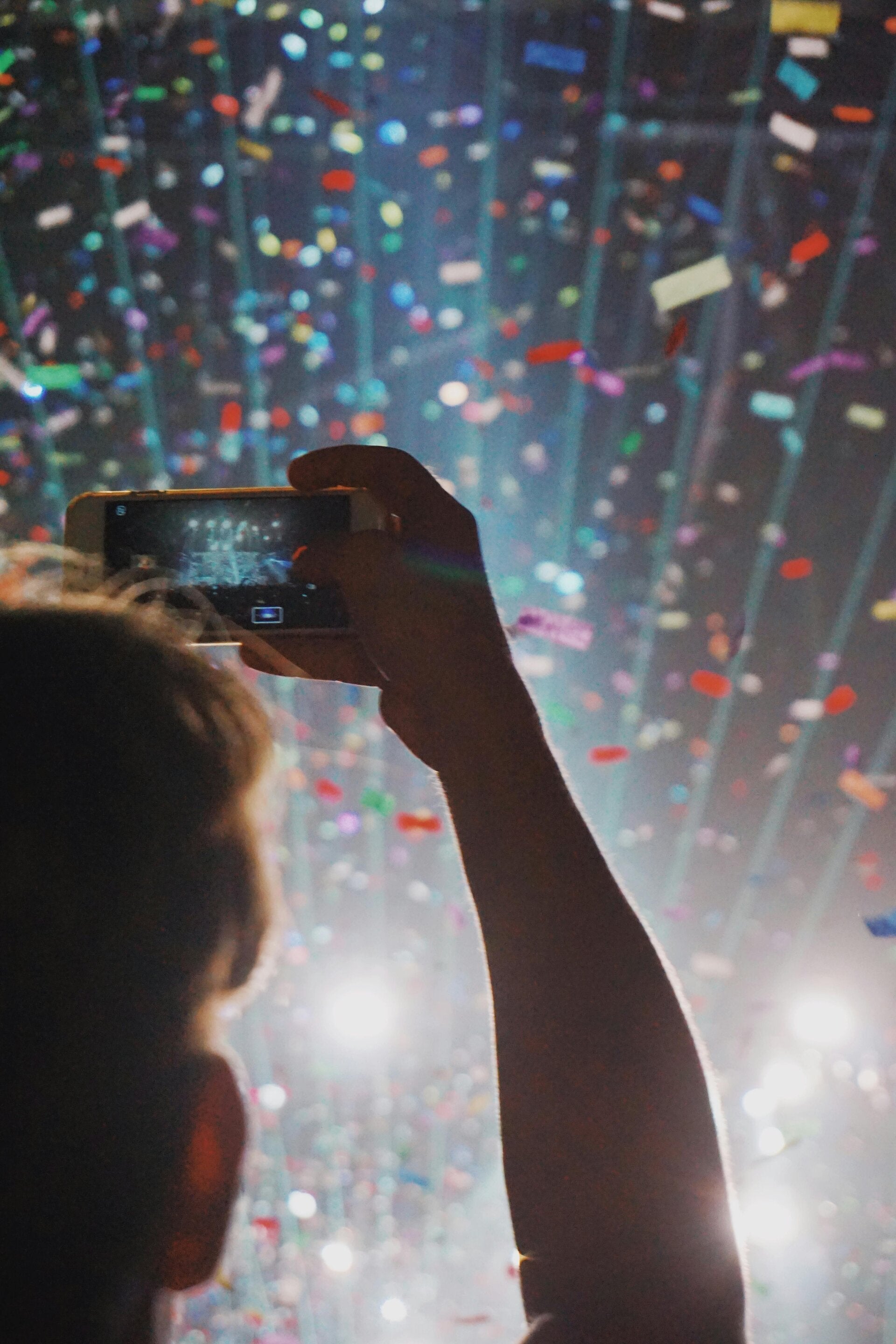Person holding phone to take photo at event with confetti and lights.