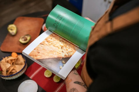 A person holding a recipe book, surrounded by a variety of foods, creating an inviting and culinary-inspired scene