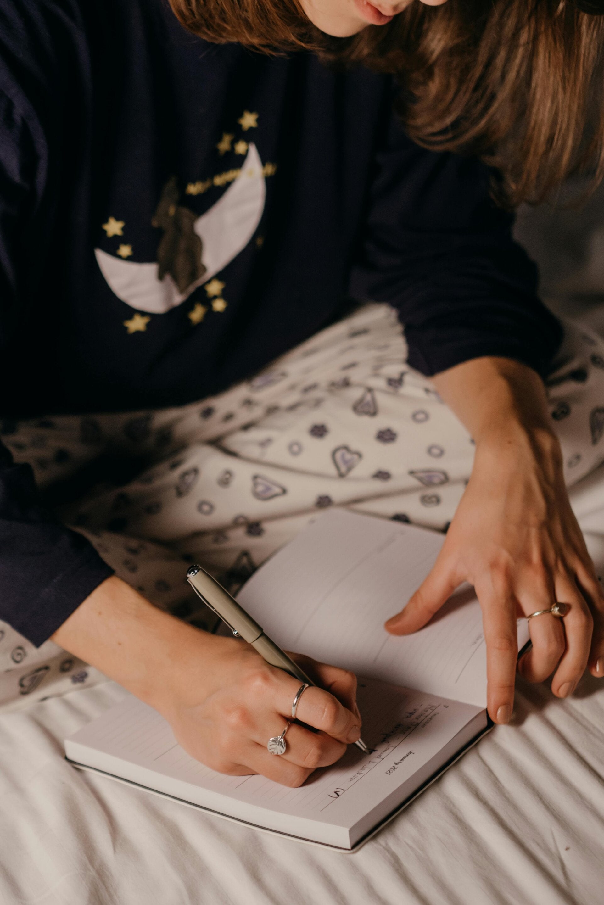 Close-up of a woman in pajamas writing in her journal, symbolizing self-reflection, comfort, and early morning personal growth.