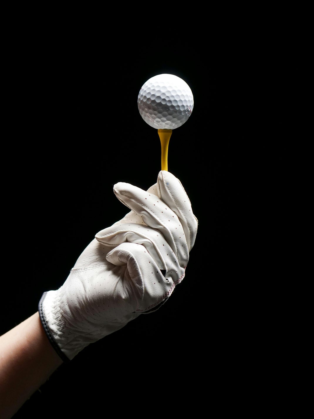 An image of a golf ball being held on the tee by a hand wearing a golf glove