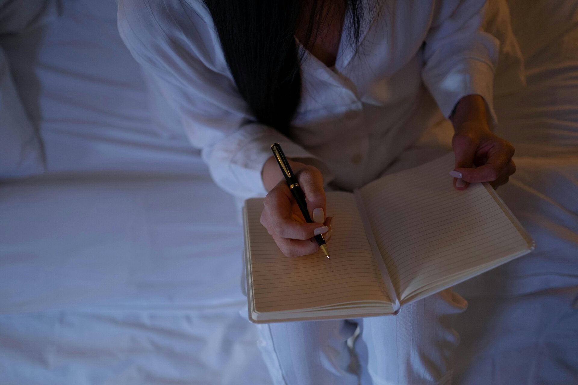 A woman journaling in bed at night by soft light, capturing a quiet moment of self-reflection, healing, and spiritual release.