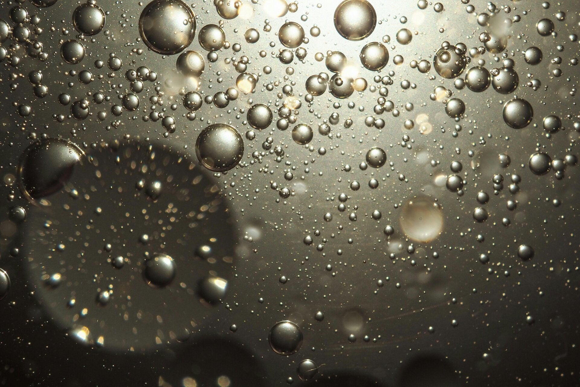 Bubbles moving up thorugh water. The image is a darker grey tint at the bottom moving through to lighter shades at the top.