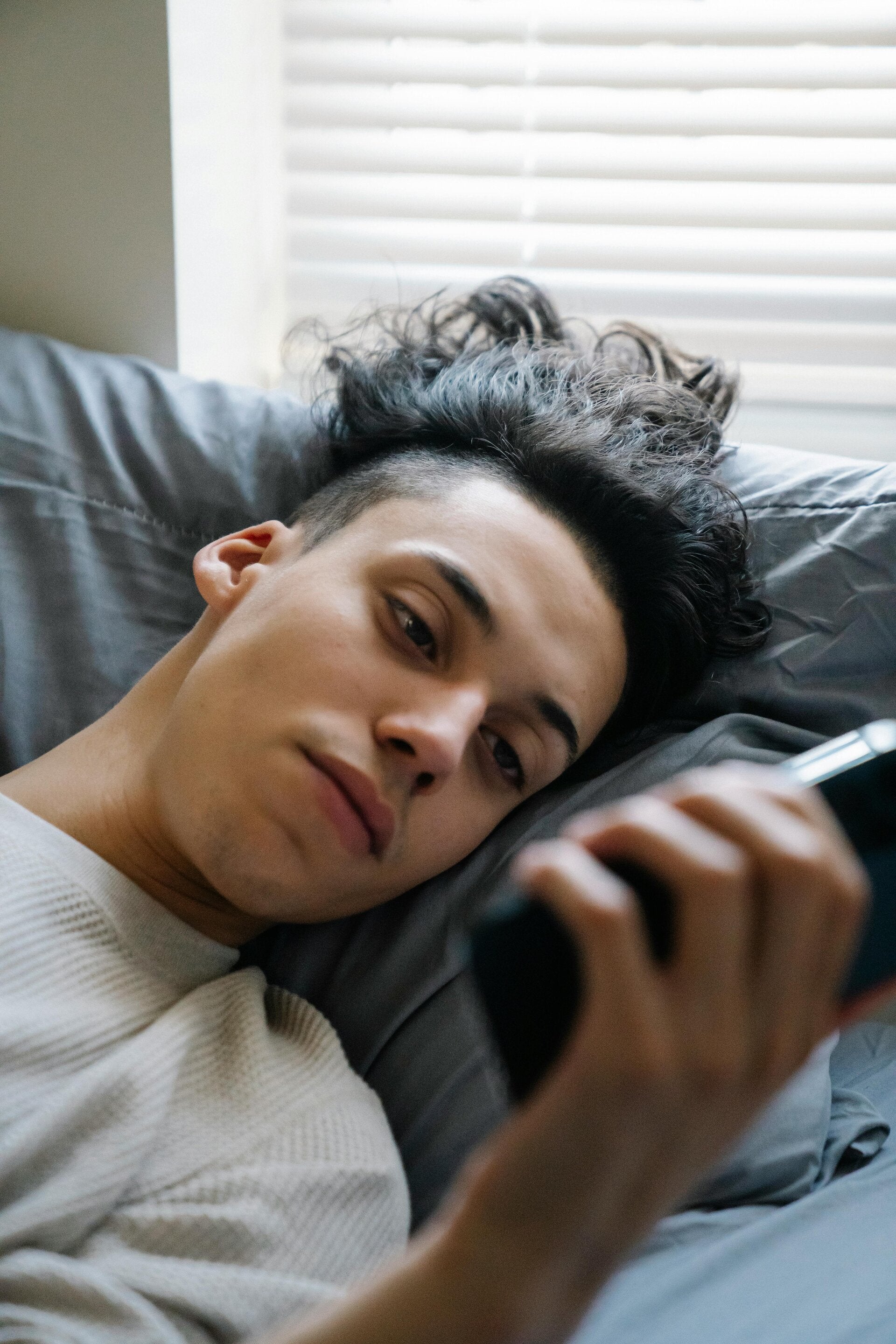 Teenage boy looking at his phone in bed in the morning, representing digital distraction and reactive habits
