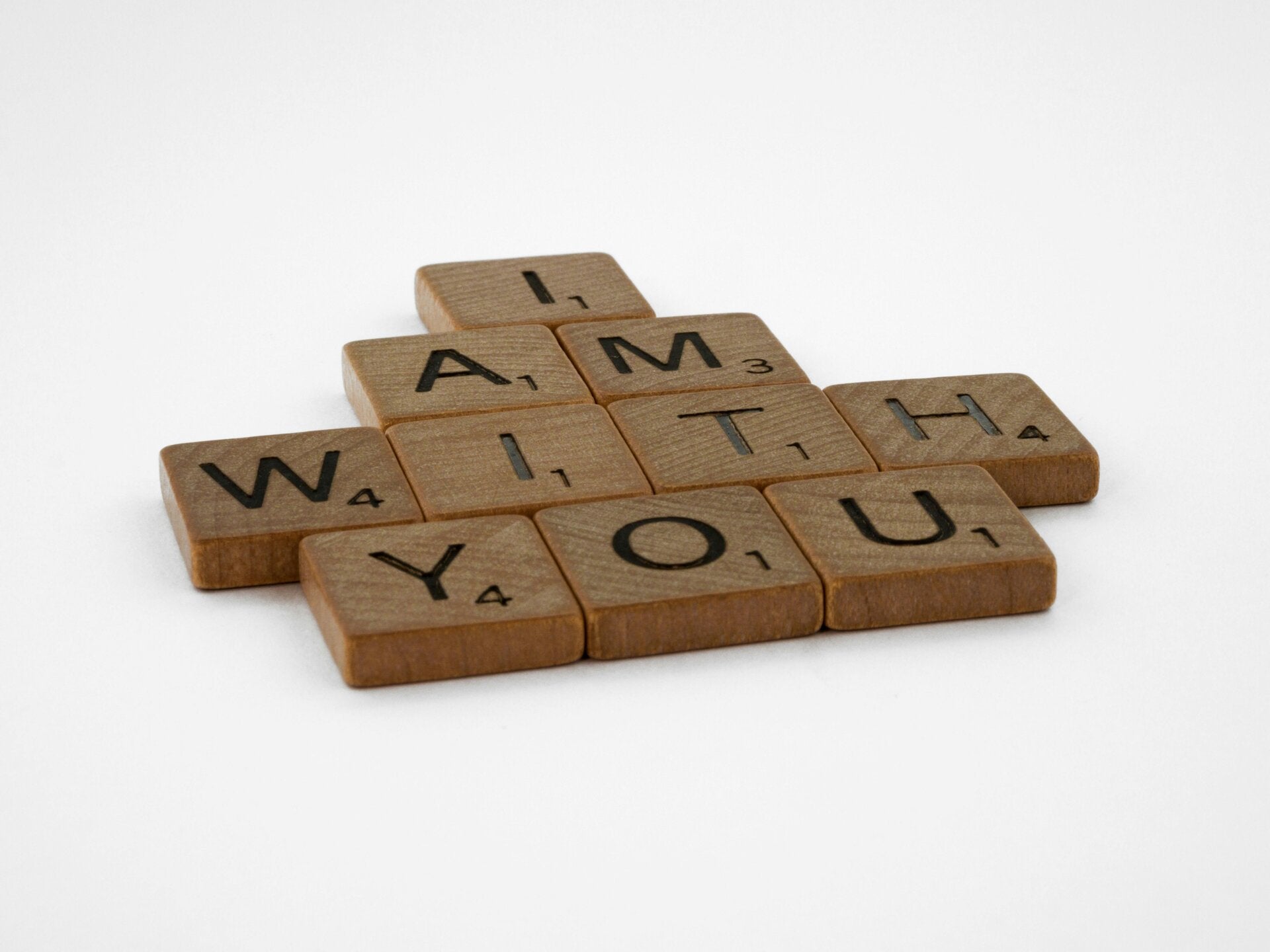 Wooden letter tiles on a white surface spelling out the phrase "I AM WITH YOU".