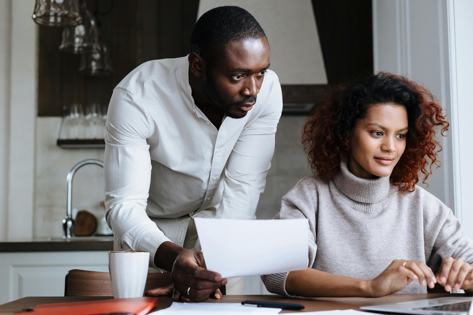 Young parents reviewing life insurance options with a laptop and coffee at a cozy kitchen table.