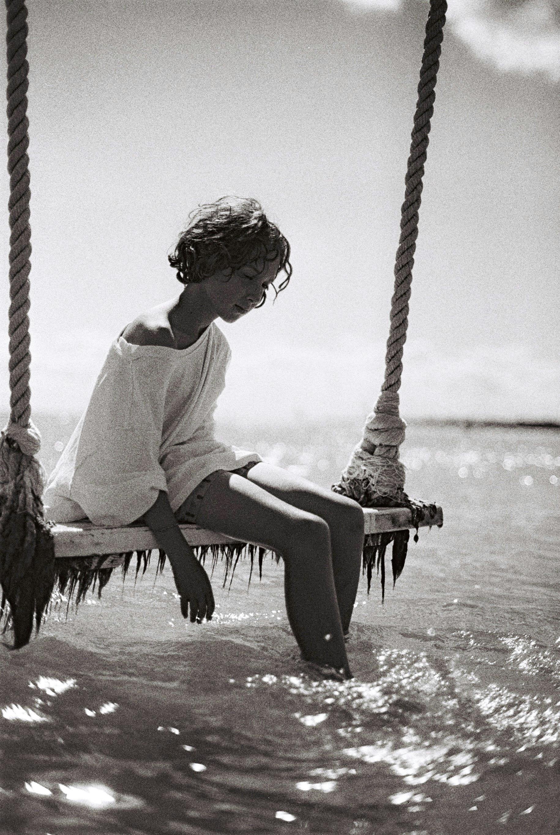 femme se balançant sur une balaçoire, air triste, la mer en trame de fond, photo noir et blanc