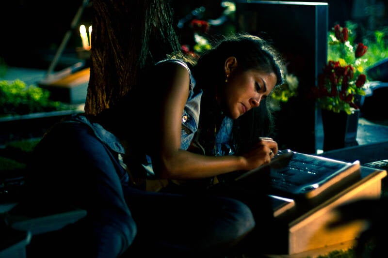 Night scene lit by candlelight, a woman leaning over a headstone