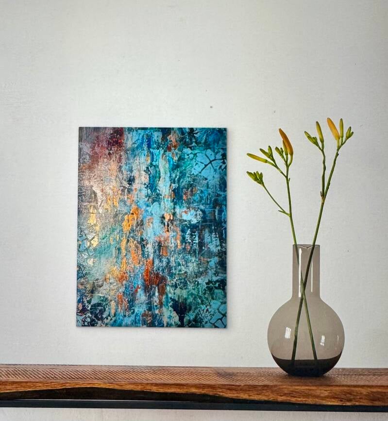 Aan de wand hangt een abstract schilderij in de kleuren blauw en koper.