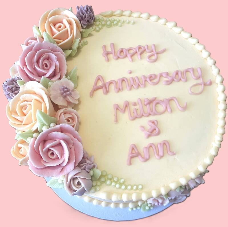 Anniversary cake decorated with pastel coloured buttercream flowers & a written message.