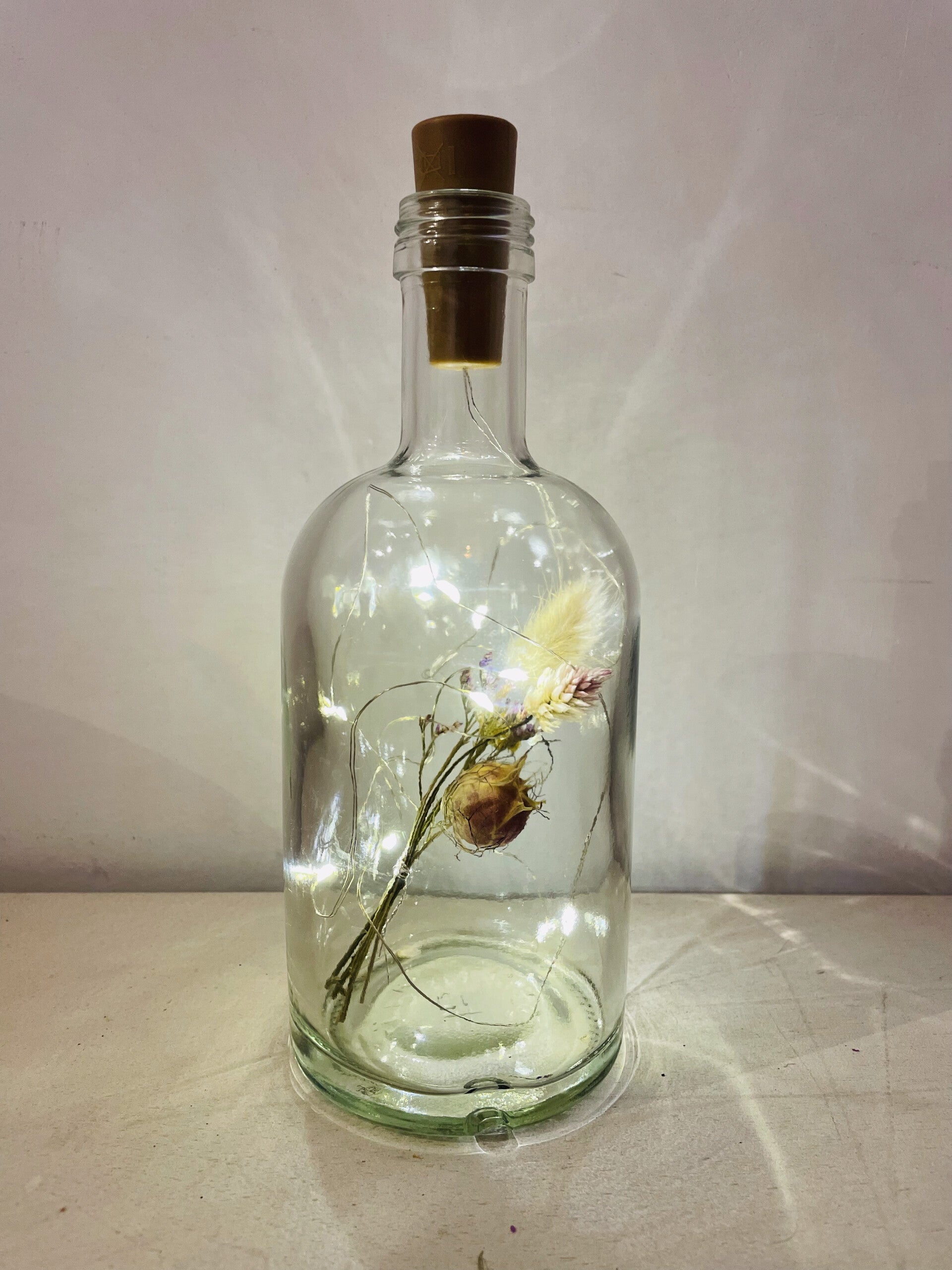 Glazen fles met droogbloemen en lichtjes
