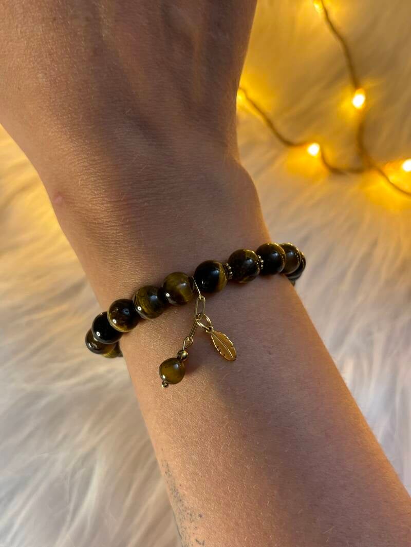 Bracelet en pierres noires porté au poignet, pampille dorée, ambiance chaleureuse et lumière douce