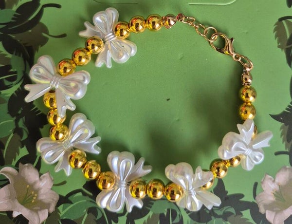 Prachtige armband met strikjes en gouden kralen en een verlengkettinkje.