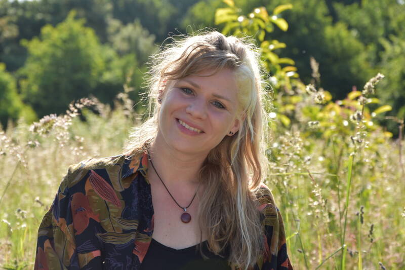 Illustrator kijkt je aan vanuit een plek in de natuur.