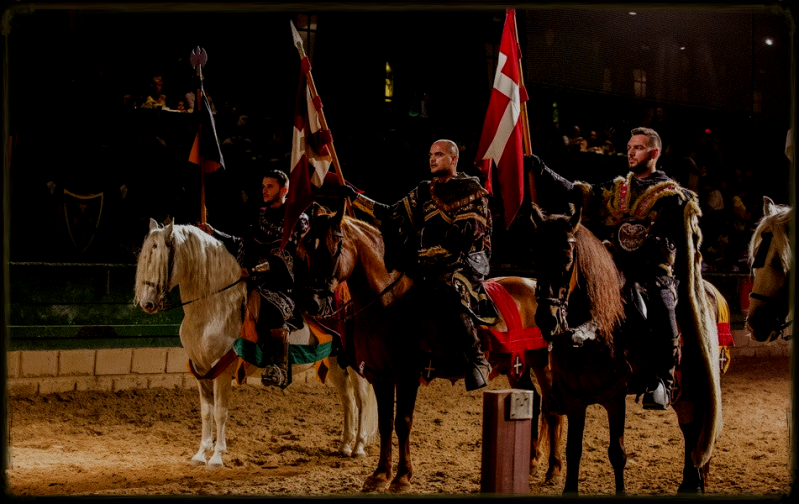 Presentacion de tre caballeros montados en caballo con sus estadartes presentandose en un torneo de justas