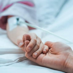 Man holding a woman’s hand with an IV in hospital, symbolizing how a critical illness policy can provide financial stability during health challenges