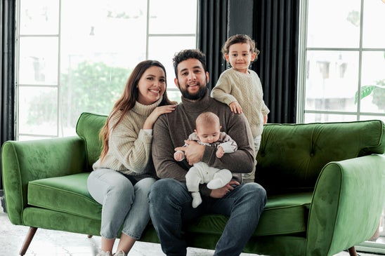 Young family sitting together on a retro style green couch in a modern design living room, representing peace of mind and protection for the future.