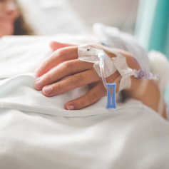 Hand with IV in hospital setting, blurred background, symbolizing how accidental benefits can enhance a primary life insurance policy during unexpected events