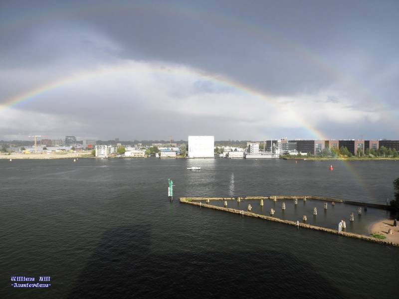 it is raining with a small rainbow in front of the house