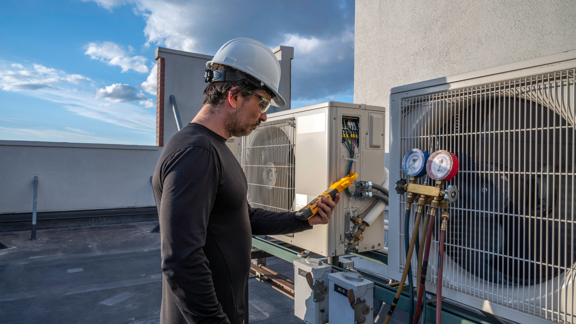 Professional HVAC technician on a building rooftop in daylight, taking amperage on a mini-split ductless air conditioning system