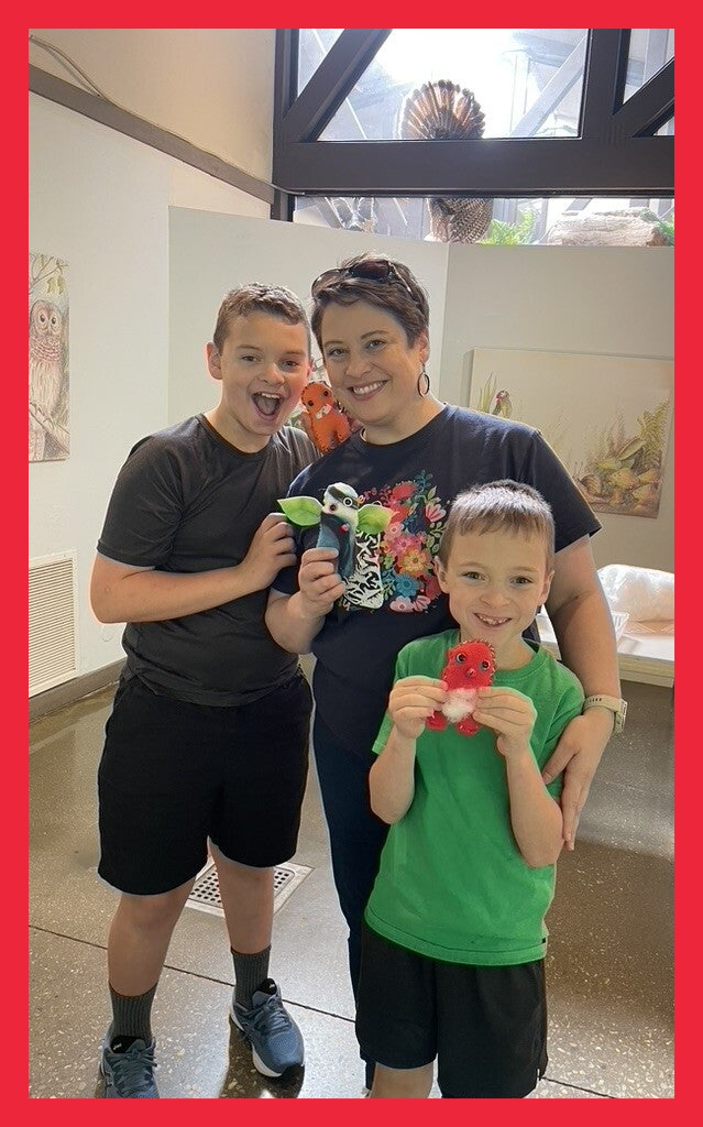 Two children and an adult smiling and holding colorful handmade monsters at a monster-making workshop.