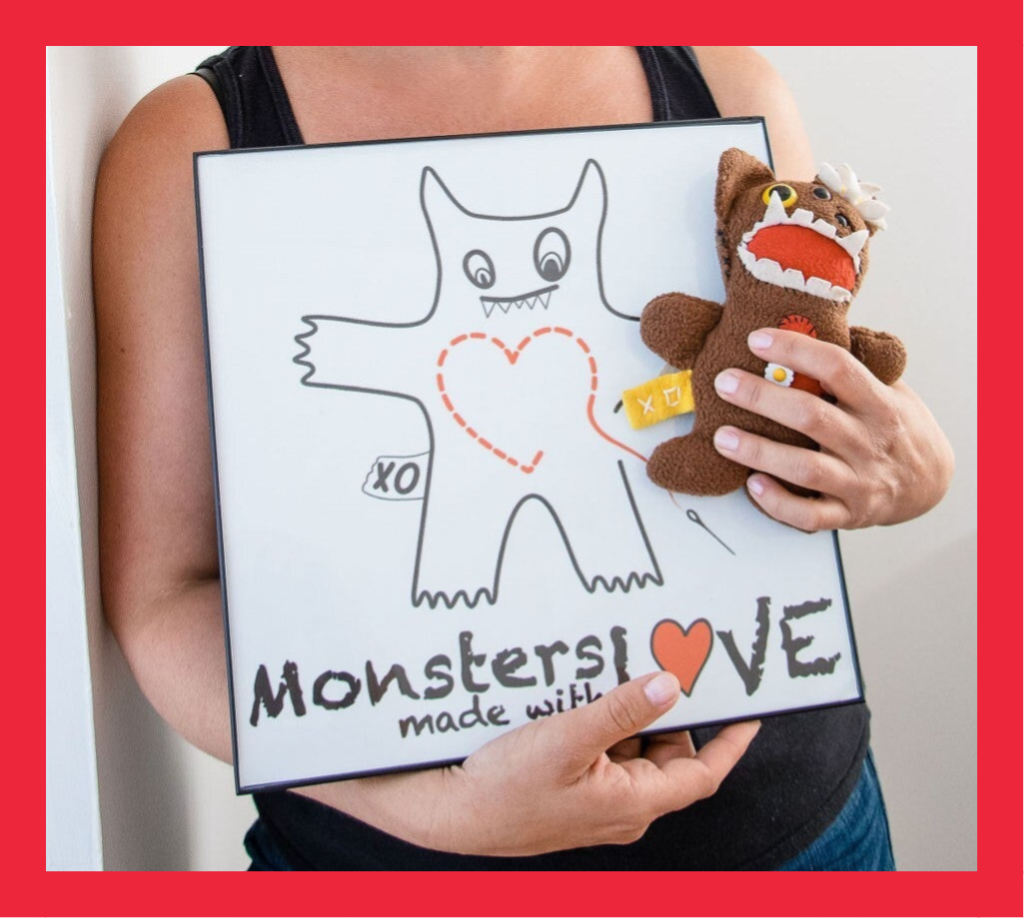 Person holding a handmade monster and a drawing featuring the Monsters Made with Love logo.