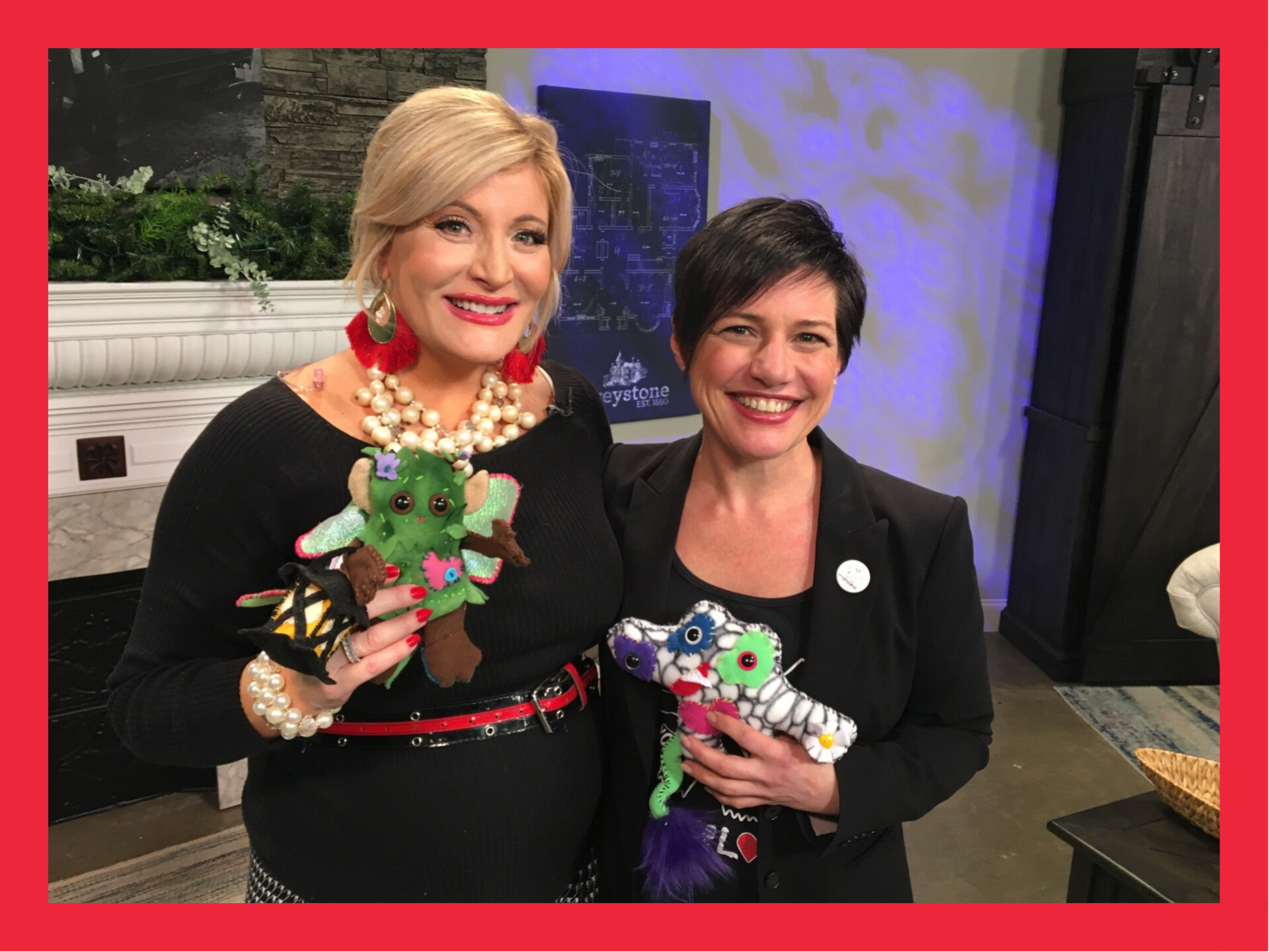 Laurie standing with another woman, both smiling and holding colorful handmade monsters at an event.